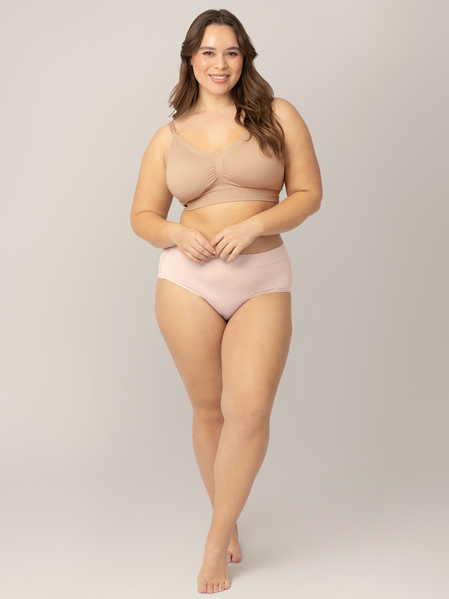 Model wearing the Grow with Me™ Maternity & Postpartum Brief in soft pink with her hands near her stomach.