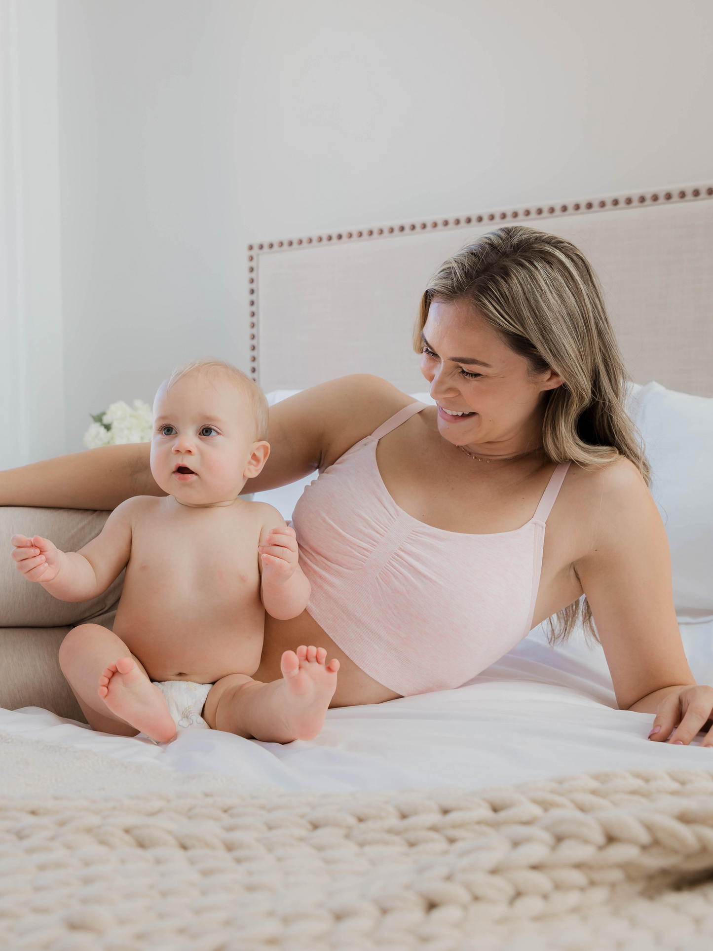 Model lounging on bed next to baby, wearing the Sublime® Bamboo Hands-Free Pumping Lounge & Sleep Bra in pink heather