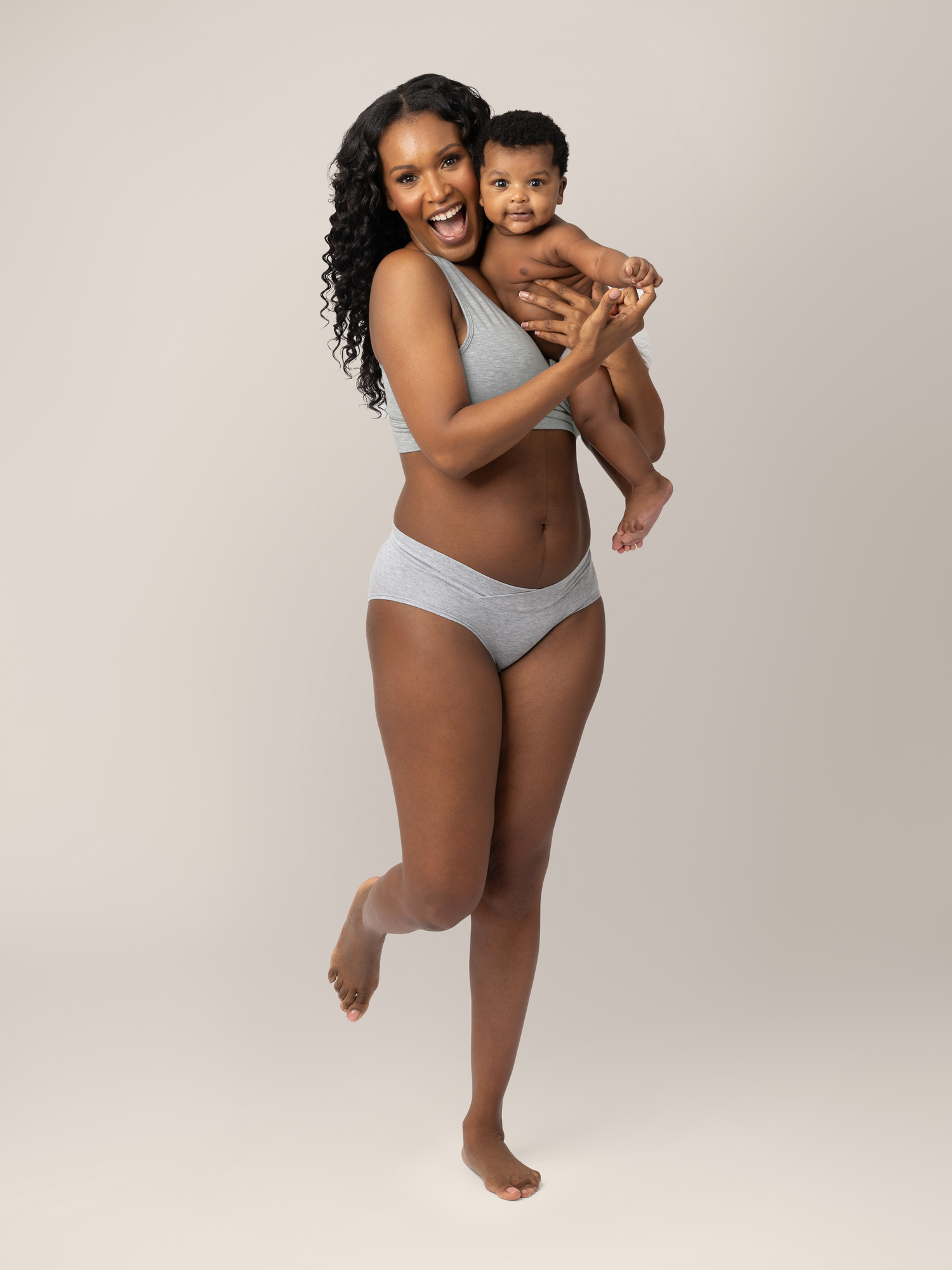 Model wearing the  Bamboo Maternity & Postpartum Hipster in Grey Heather with her baby on her hip smiling.