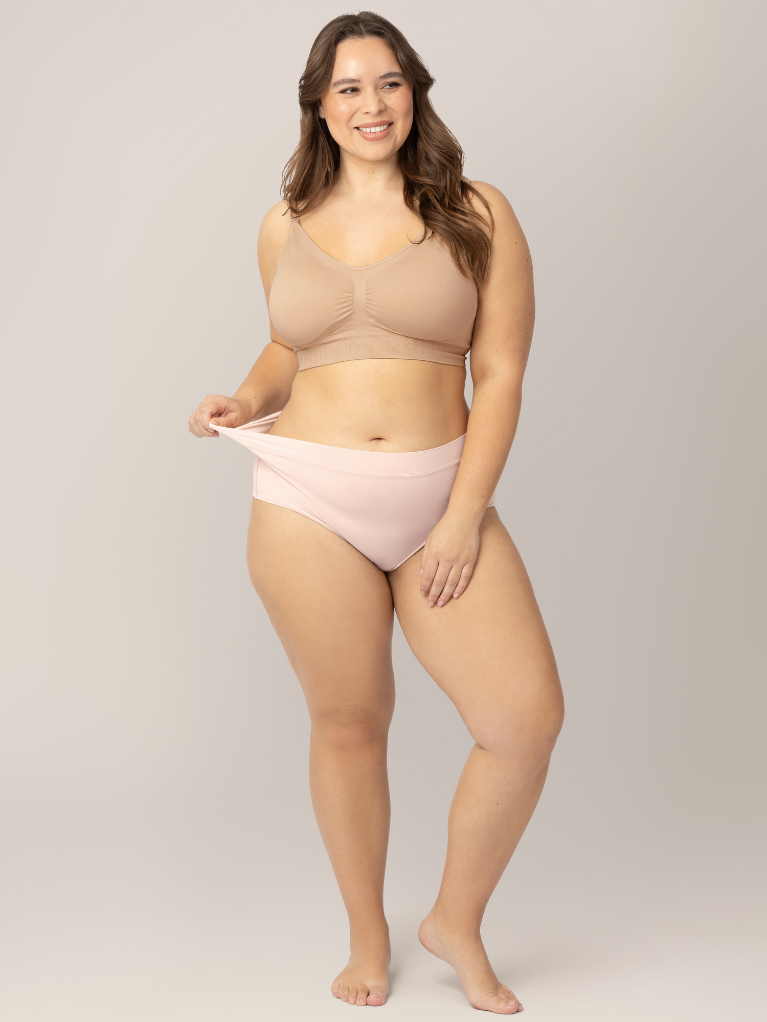Model wearing the Grow with Me™ Maternity & Postpartum Brief in Soft Pink holding onto the waistband to show the elasticity.