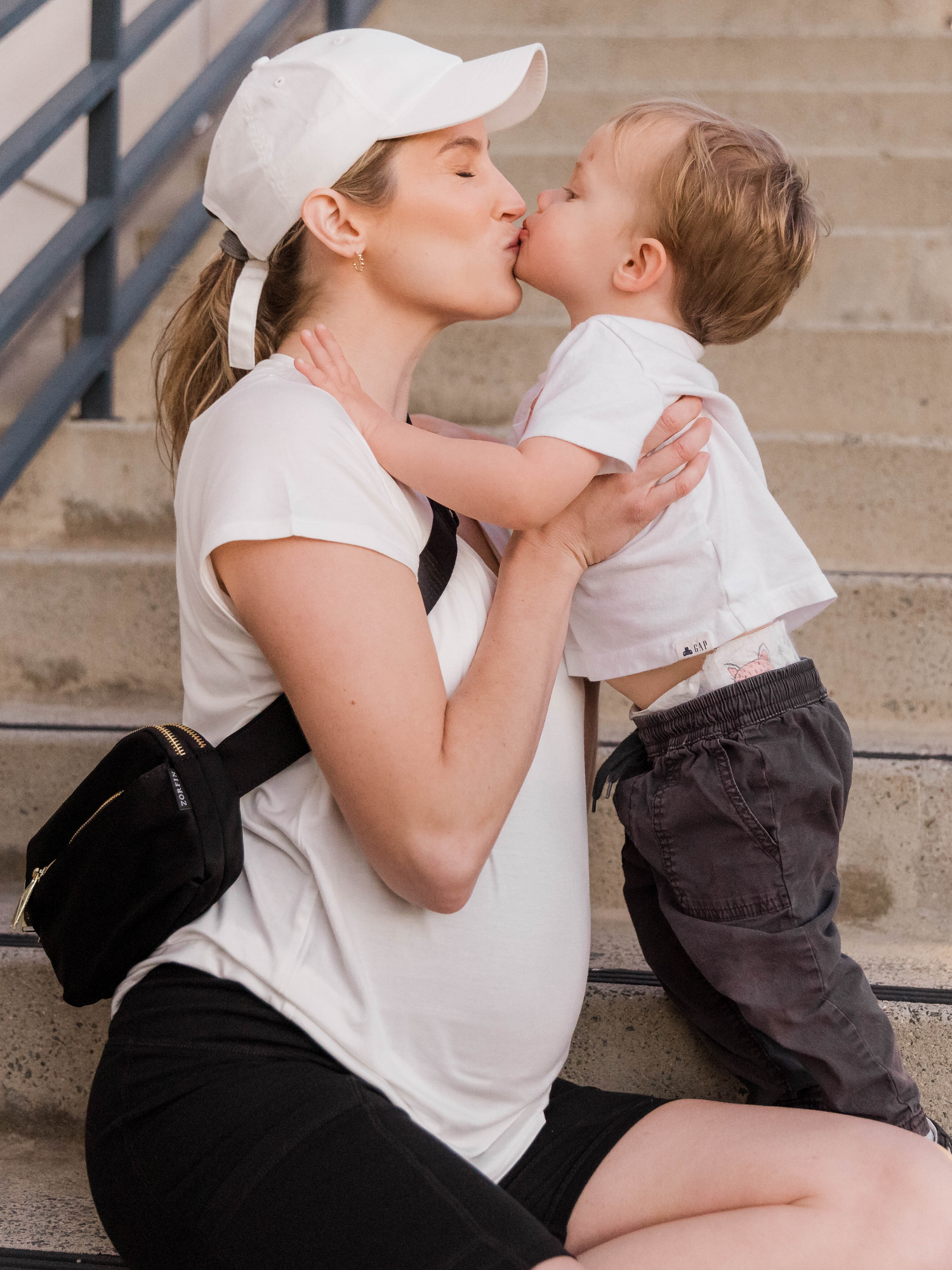 Pregnant model kissing her child whiel wearing the Everyday Maternity & Nursing T-shirt in White on stairs.