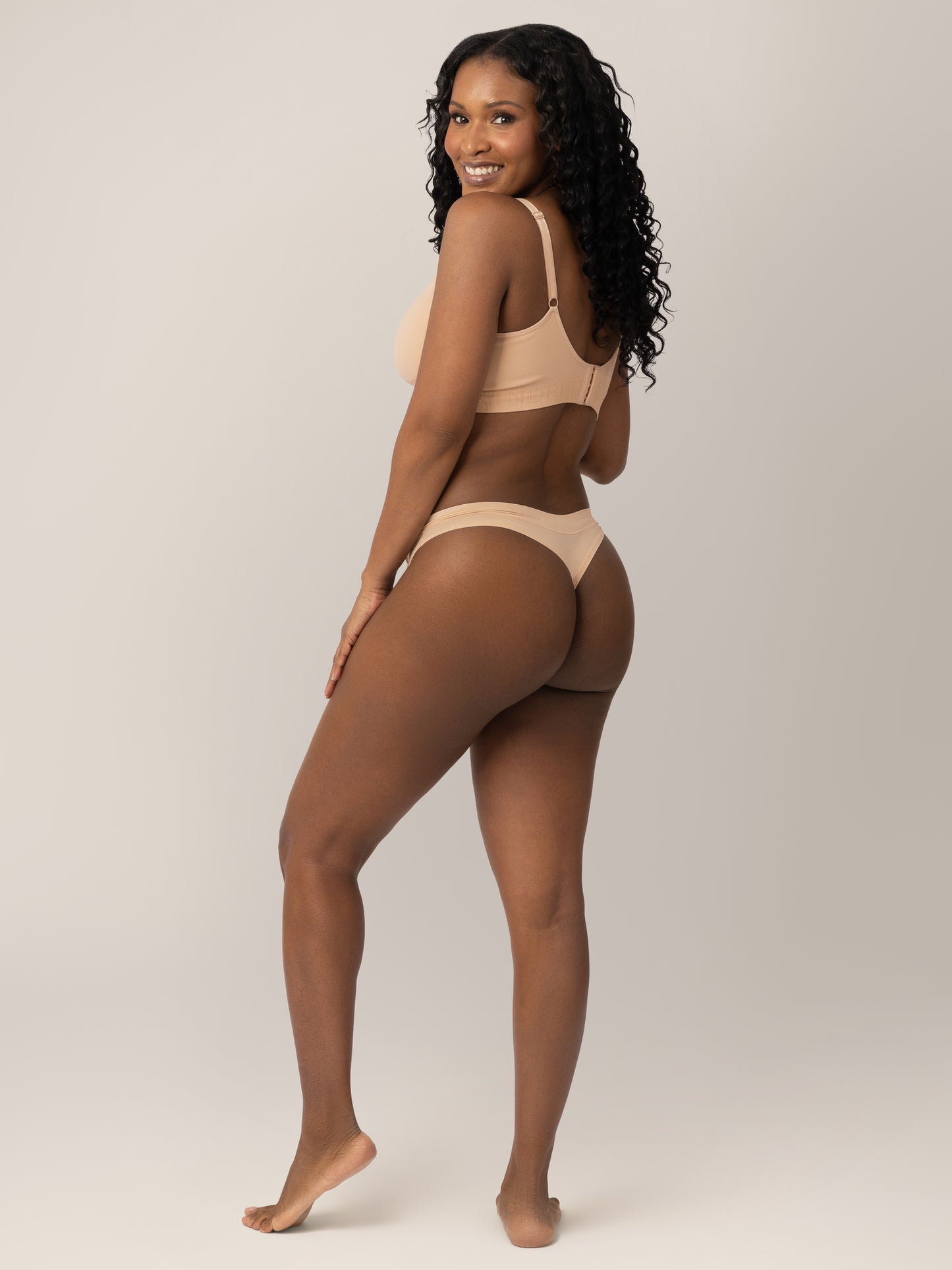 Back of a model wearing the Grow with Me™ Maternity & Postpartum Thong in Beige with her hand on her hip.