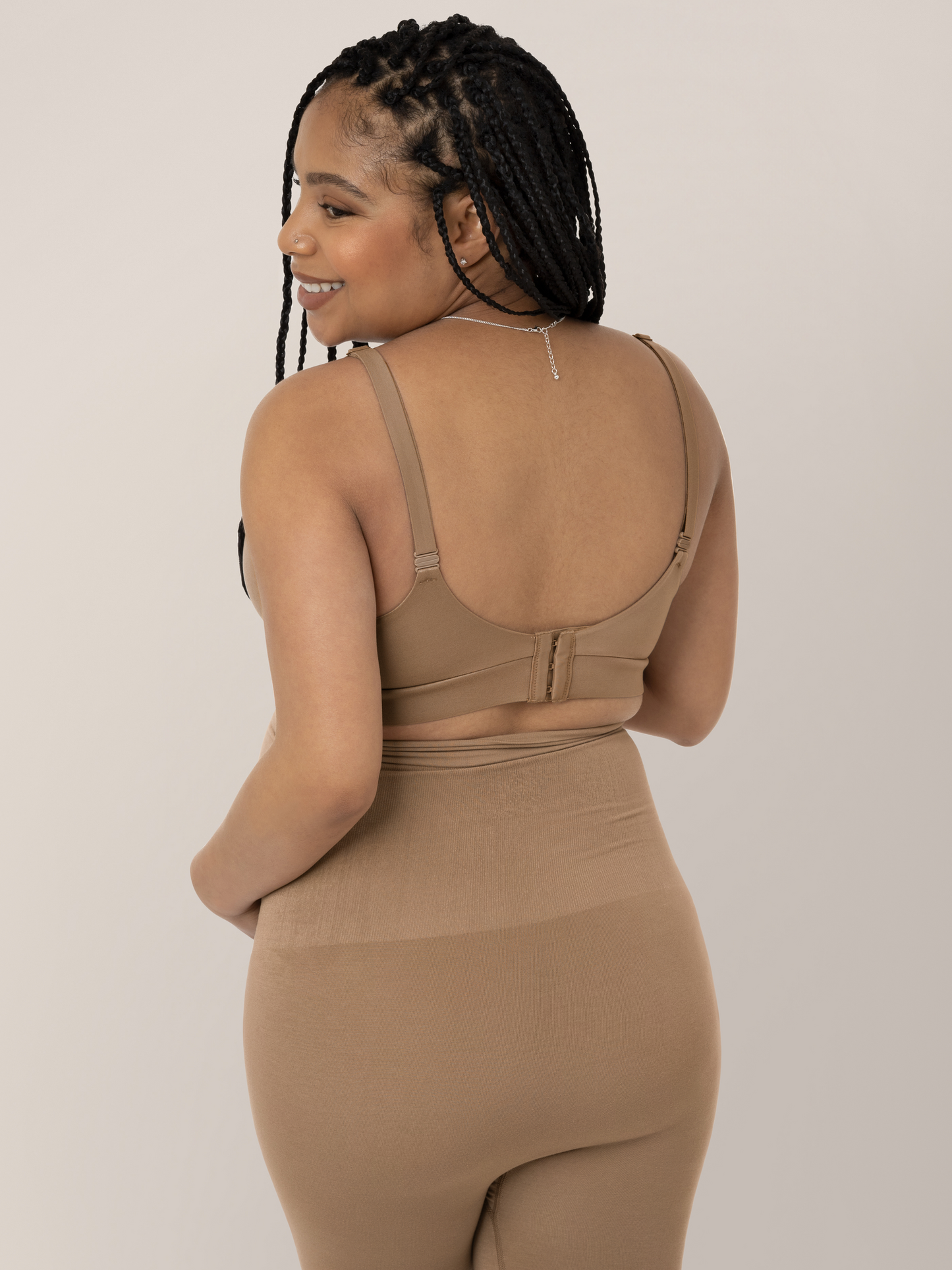 Back of a model wearing the Minimalist Hands-Free Pumping and Nursing Bra in Latte and smiling over her shoulder.