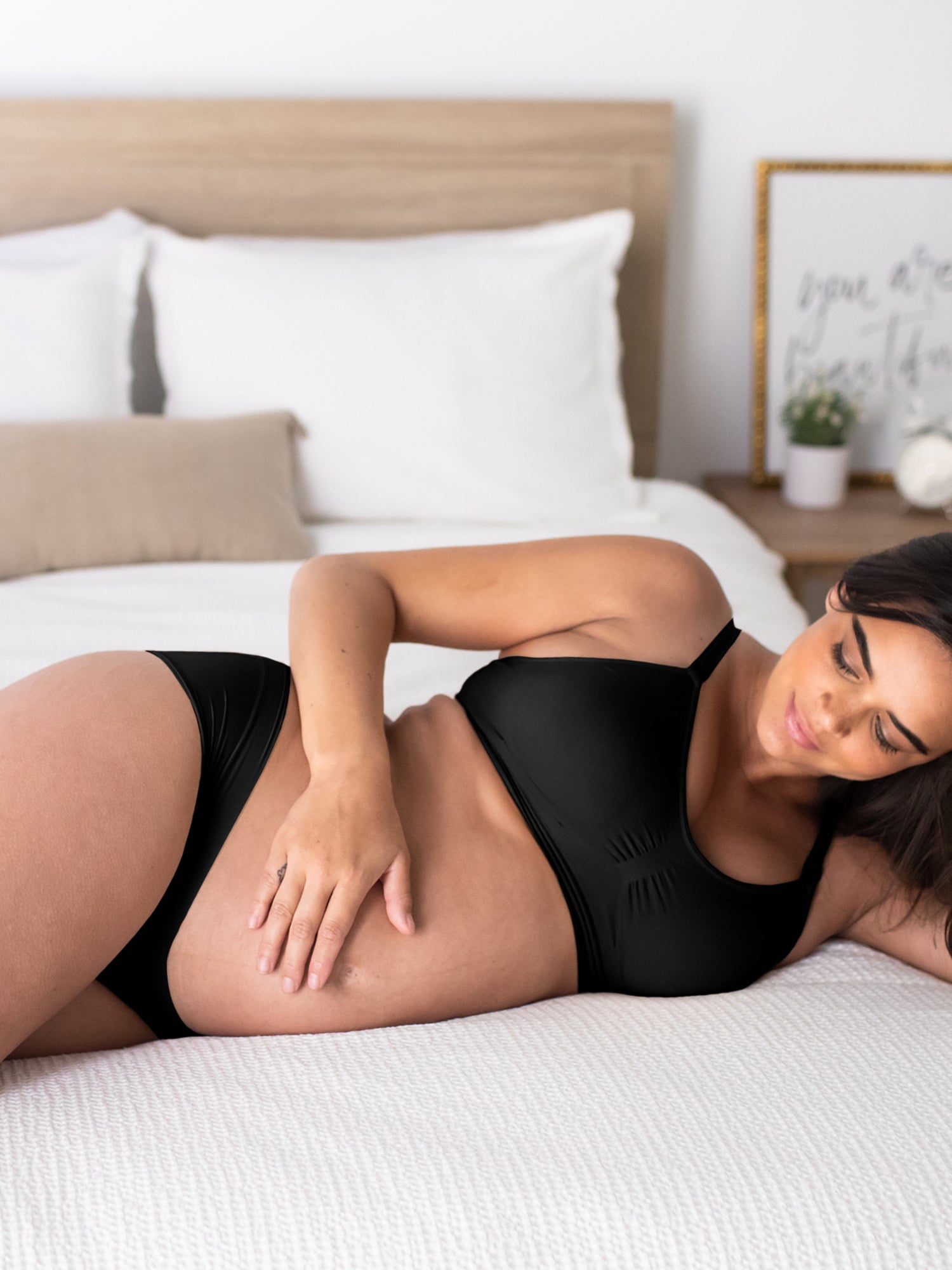 Pregnant model laying on a bed wearing the Grow with Me™ Maternity & Postpartum Hipster in Black