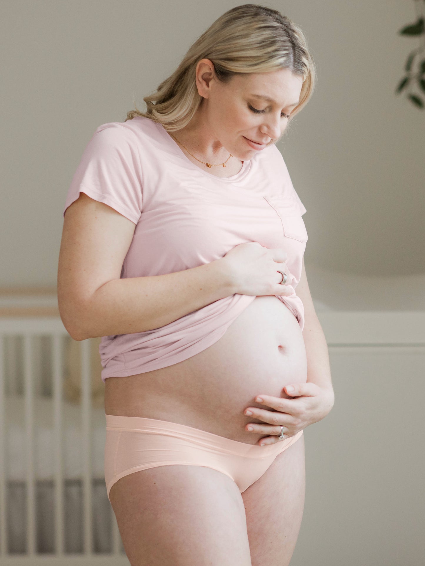Model holding her baby bump while looking down and wearing the Grow with Me™ Maternity & Postpartum Hipster in Soft Pink @model_info:Jessie is wearing Medium.