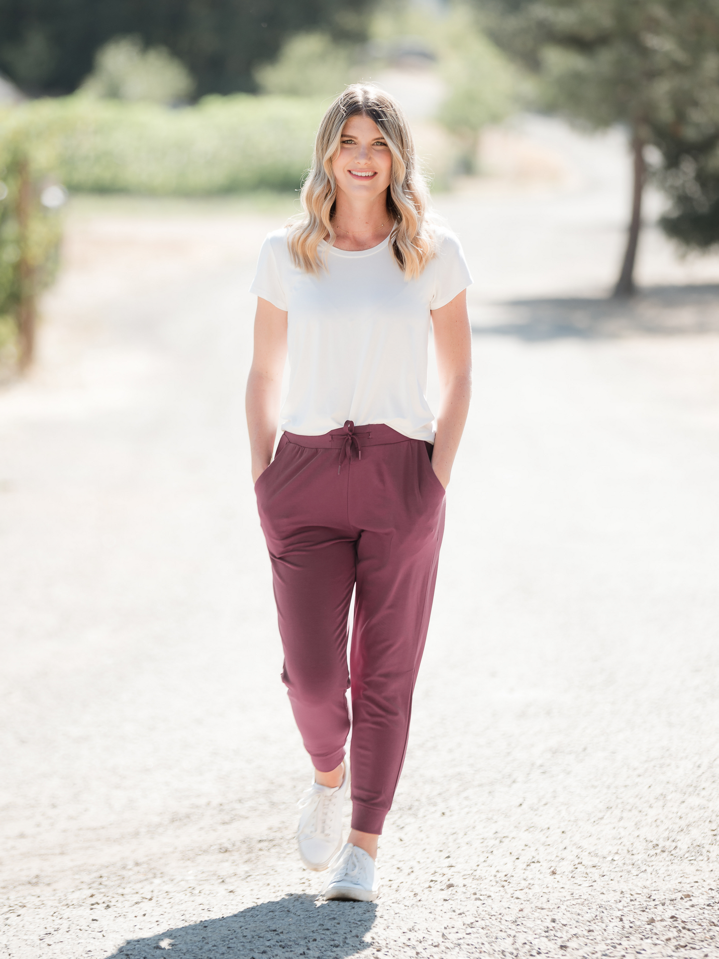 Model wearing the Bamboo Everyday T-shirt in White with her hands in the pockets of her joggers. @model_info:Amber is wearing a Small.