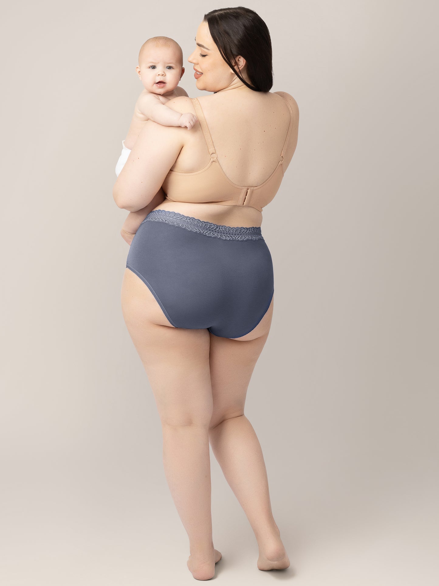 Back view of a model wearing the High Waisted Postpartum underwear in Dusty Hues holding her baby on her hip.