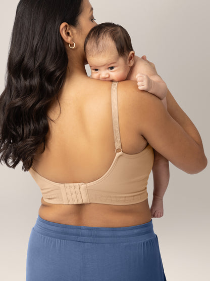 Back of a model carrying her baby while wearing Sublime® Hands-Free Pumping & Nursing Bra in Beige