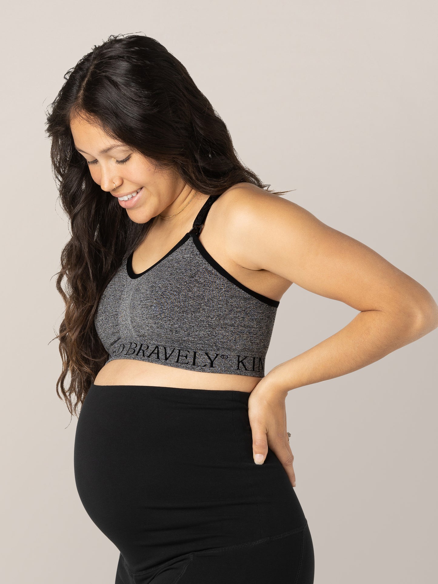 Pregnant model looking down at her baby bump while wearing the Sublime® Nursing Sports Bra in Heather Grey.