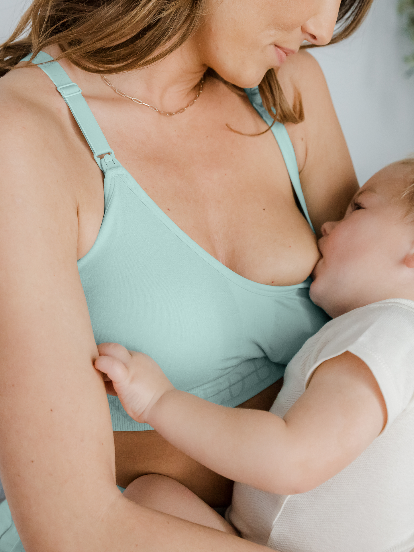 Model wearing the Sublime® Hands-Free Pumping & Nursing Sports Bra in dusty blue green and nursing baby 