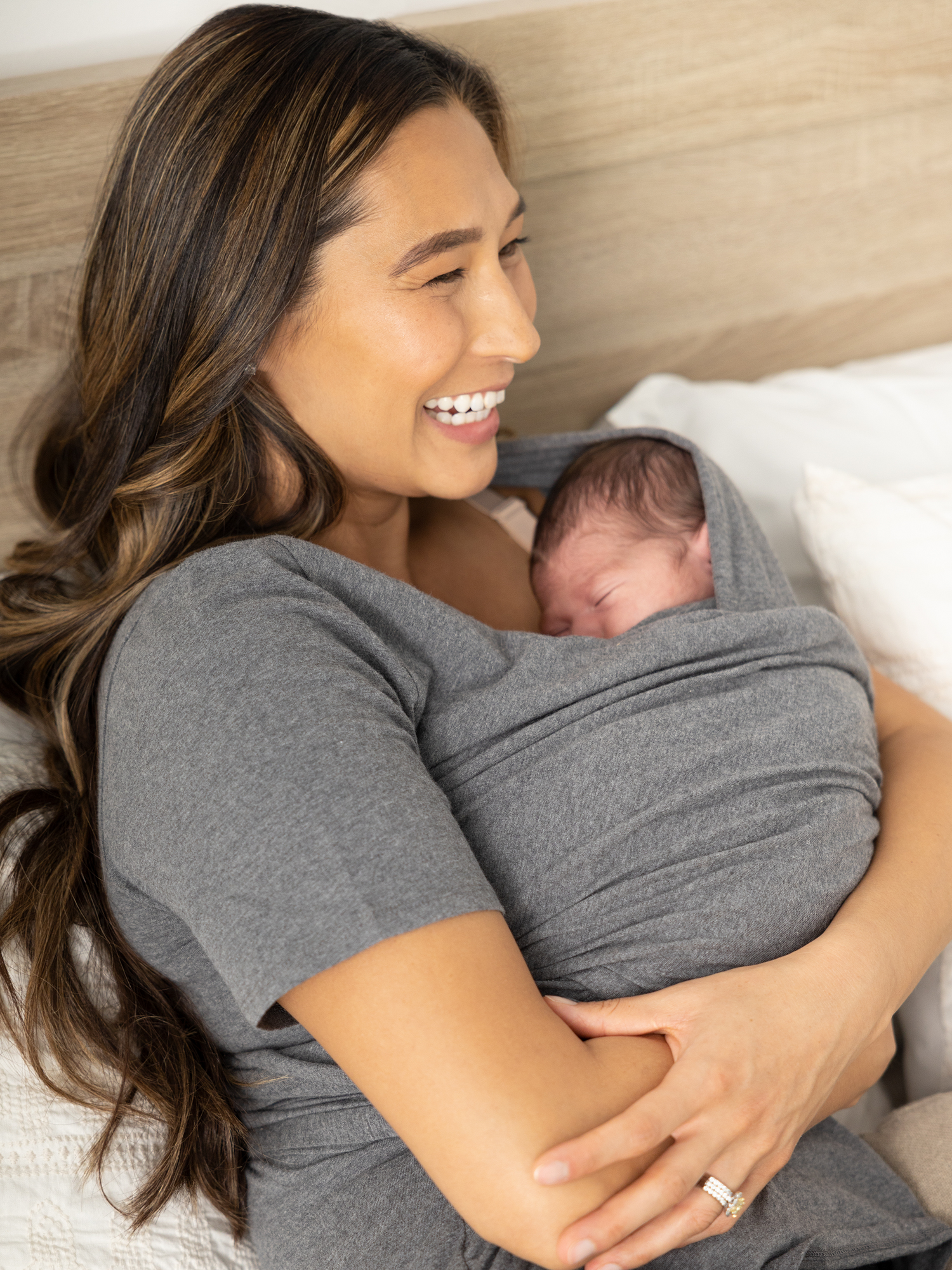 Model laying on a bed with her baby wearing the Organic Cotton Skin to Skin Wrap Top in Charcoal Grey Heather