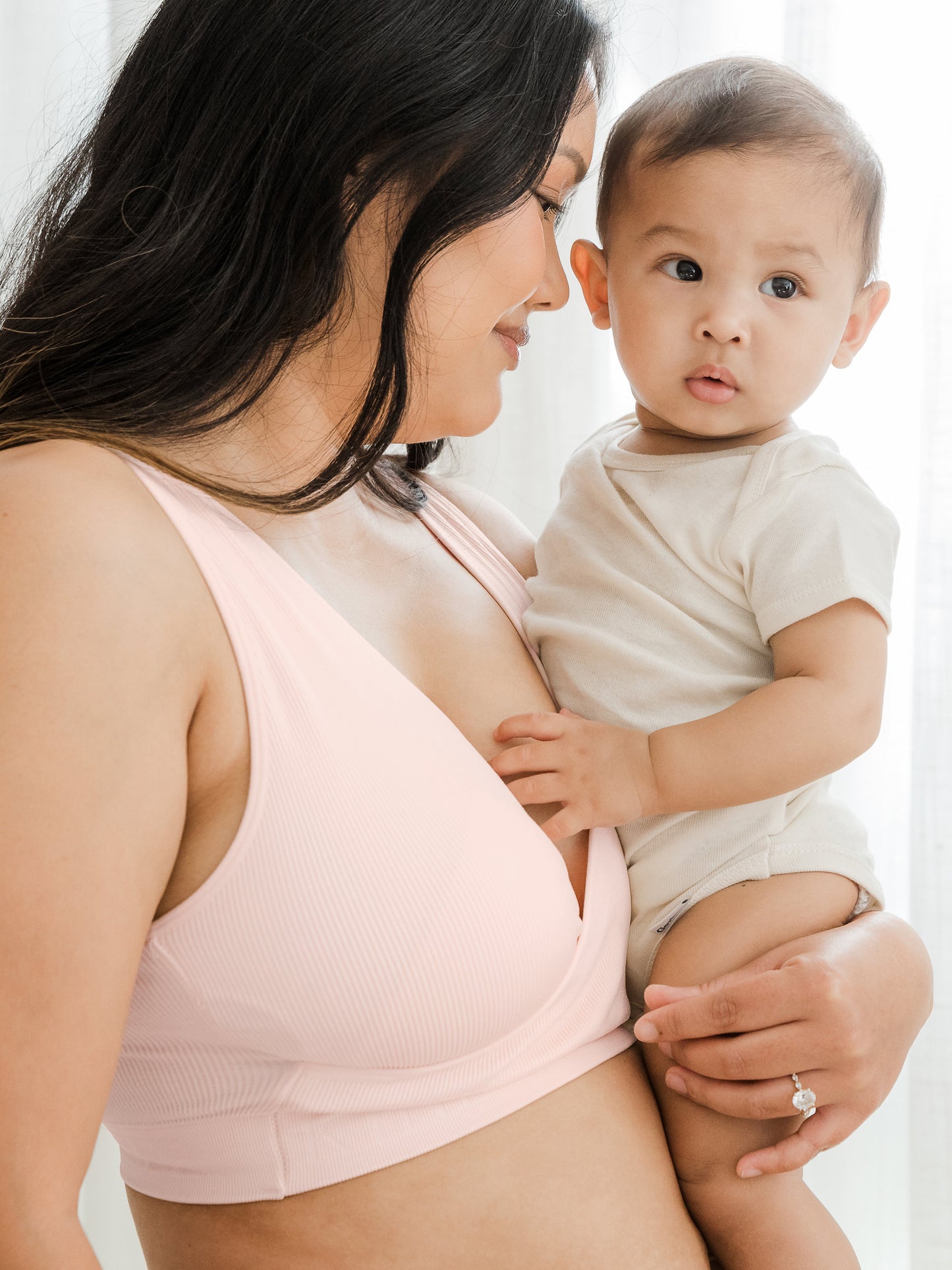 Model wearing the Sublime® Adjustable Crossover Nursing & Lounge Bra in Soft Pink with her baby on her hip. @model_info:Binc is wearing a Medium Busty.