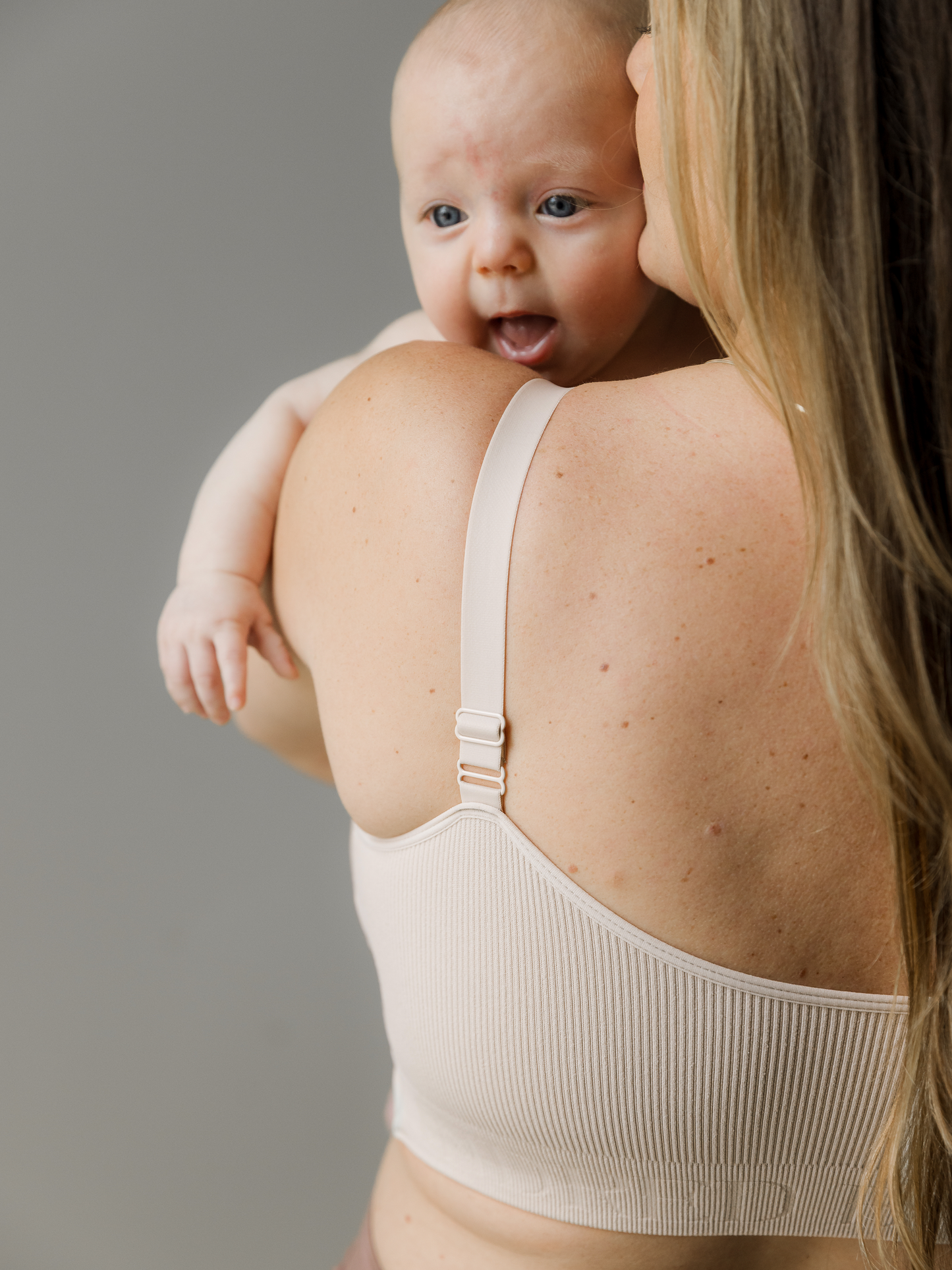 Model wearing the Sublime® Adjustable Crossover Nursing & Lounge Bra in Stone with her baby looking over her shoulder. 
