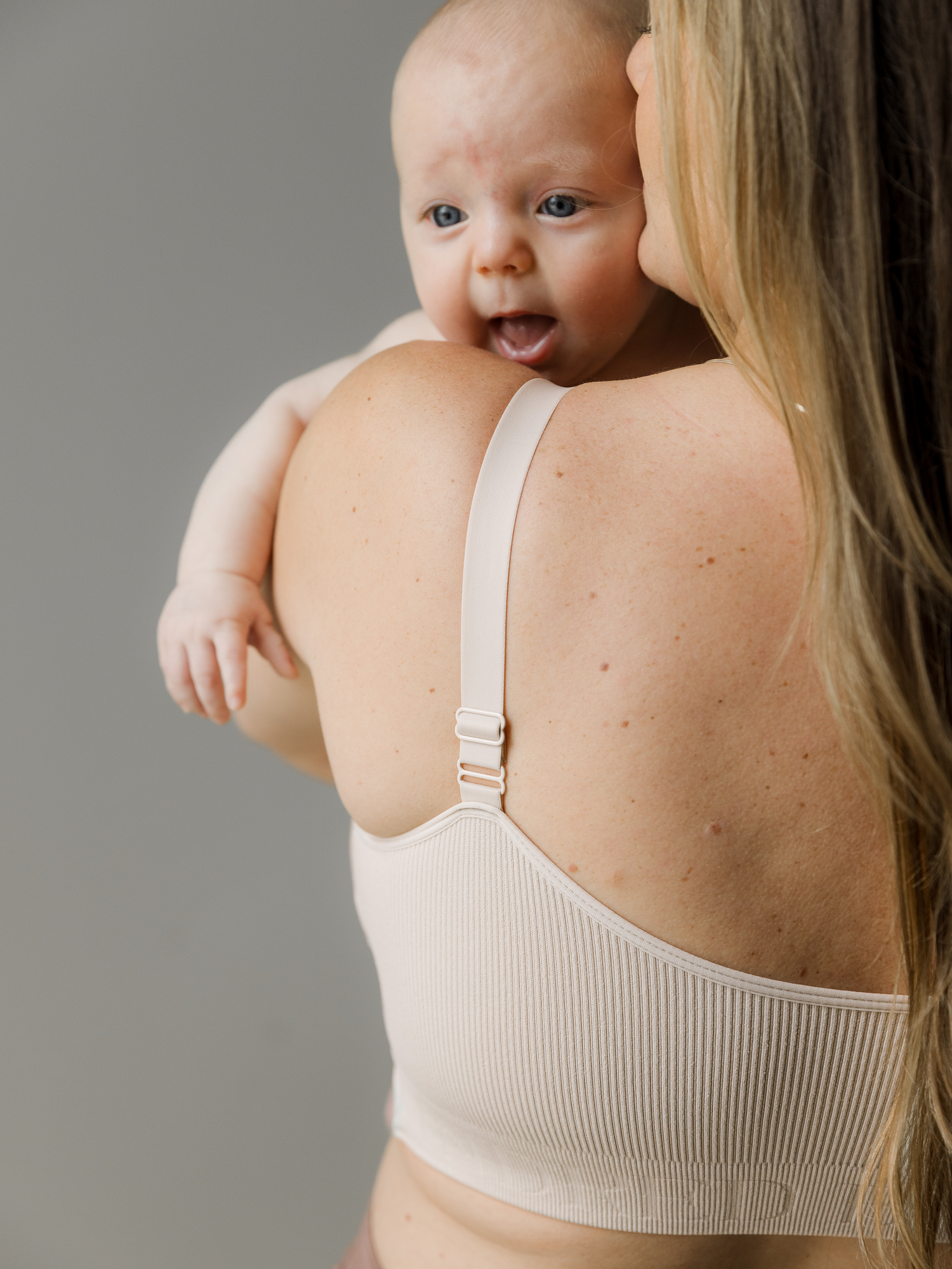 Model wearing the Sublime® Adjustable Crossover Nursing & Lounge Bra in Stone with her baby looking over her shoulder.