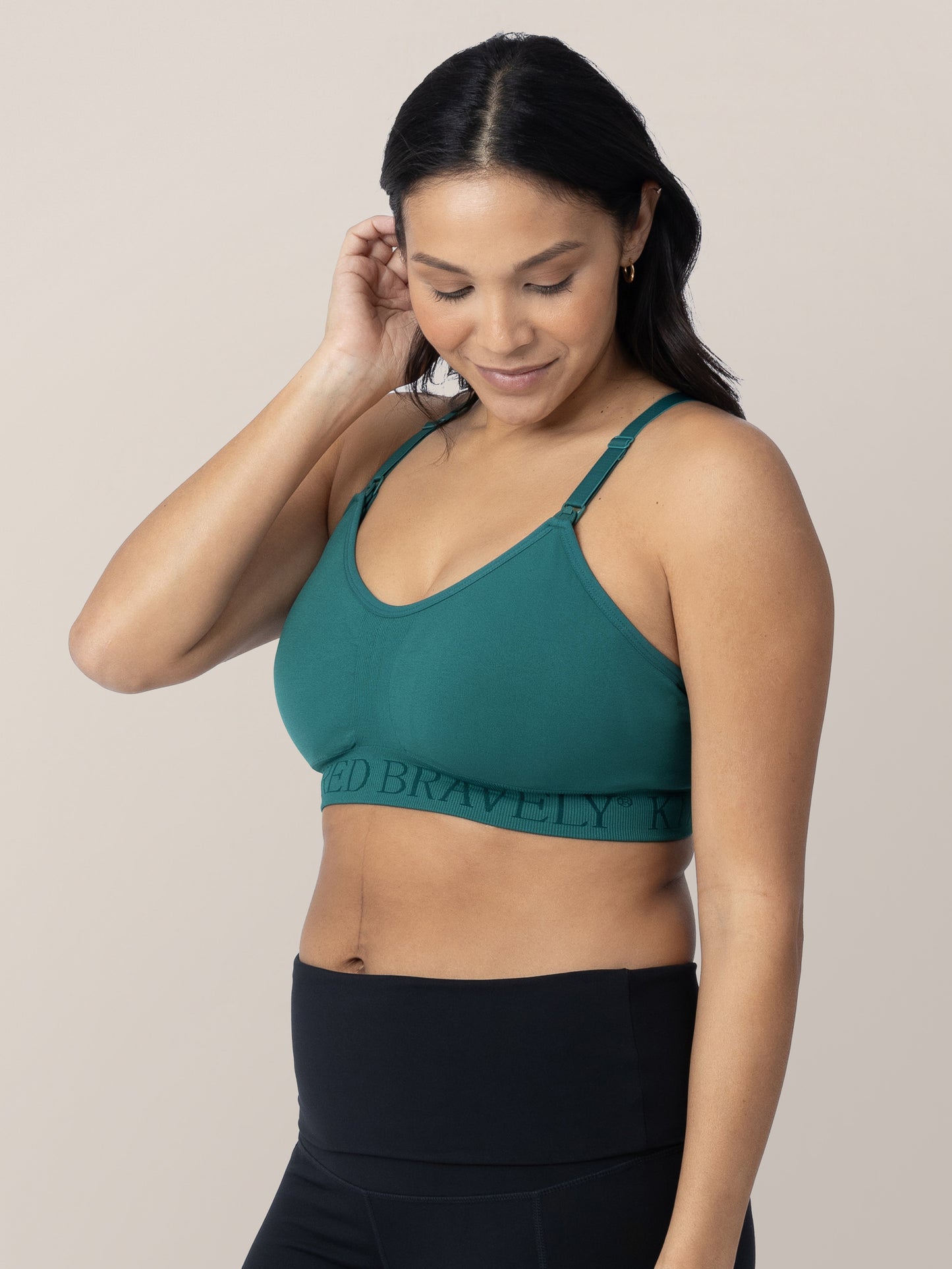 Model tucking her hair behind her ear while wearing the Sublime® Hands-Free Pumping & Nursing Sports Bra in teal.@model_info:Julana is wearing a Small.