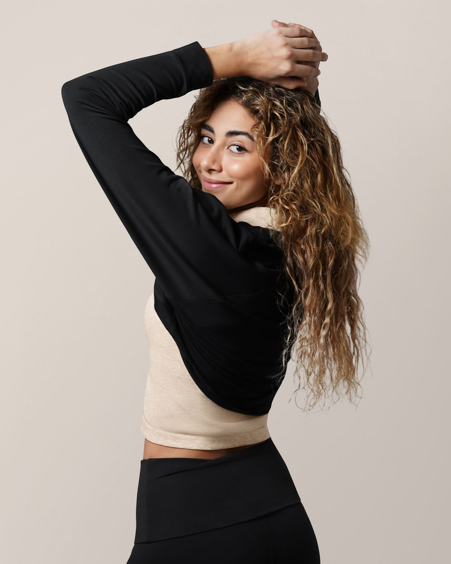 Side back view of model with both hands on head, wearing the French Terry Cardigan Shrug in Black, paired with the Sublime® Bamboo Collared Maternity & Nursing Longline Bra Top in Oatmeal Heather and Louisa Legging.