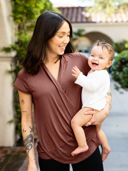 Model outside holding baby and wearing the Bamboo Draped Nursing Top in redwood @model_info:Lyn is wearing a Small.