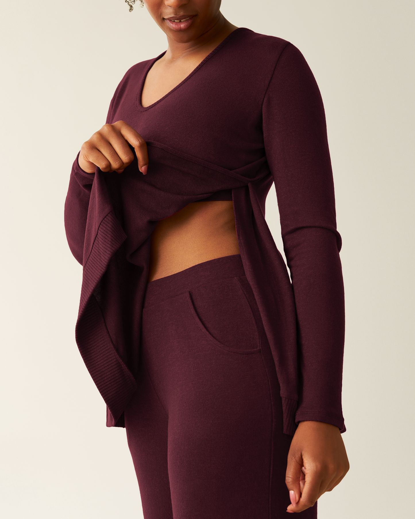 Person showing side opening of the CozyKnit Maternity & Nursing V-neck Top in Deep Burgundy with matching pants on a plain background