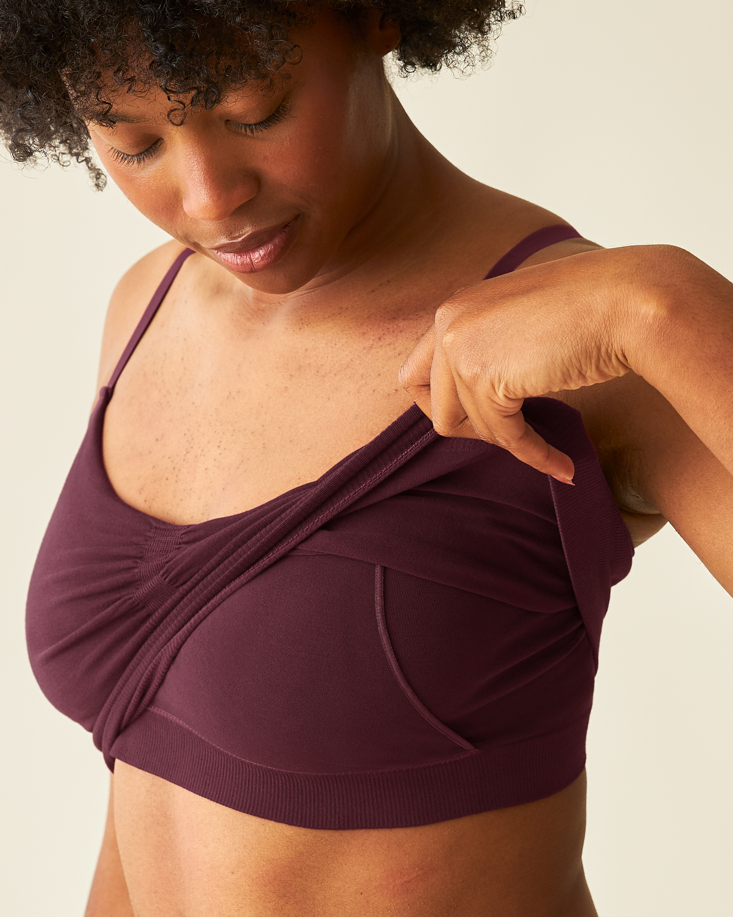 Woman wearing the Sublime® Bamboo Hands-Free Pumping Lounge & Sleep Bra in Deep Burgundy, lifting up outer layer to show pumping access