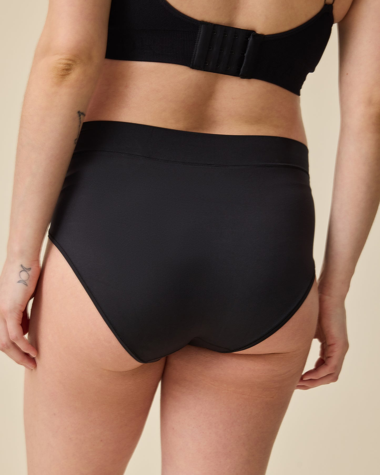 Back view of model wearing Grow with Me™ Maternity & Postpartum Brief in Black on a beige background