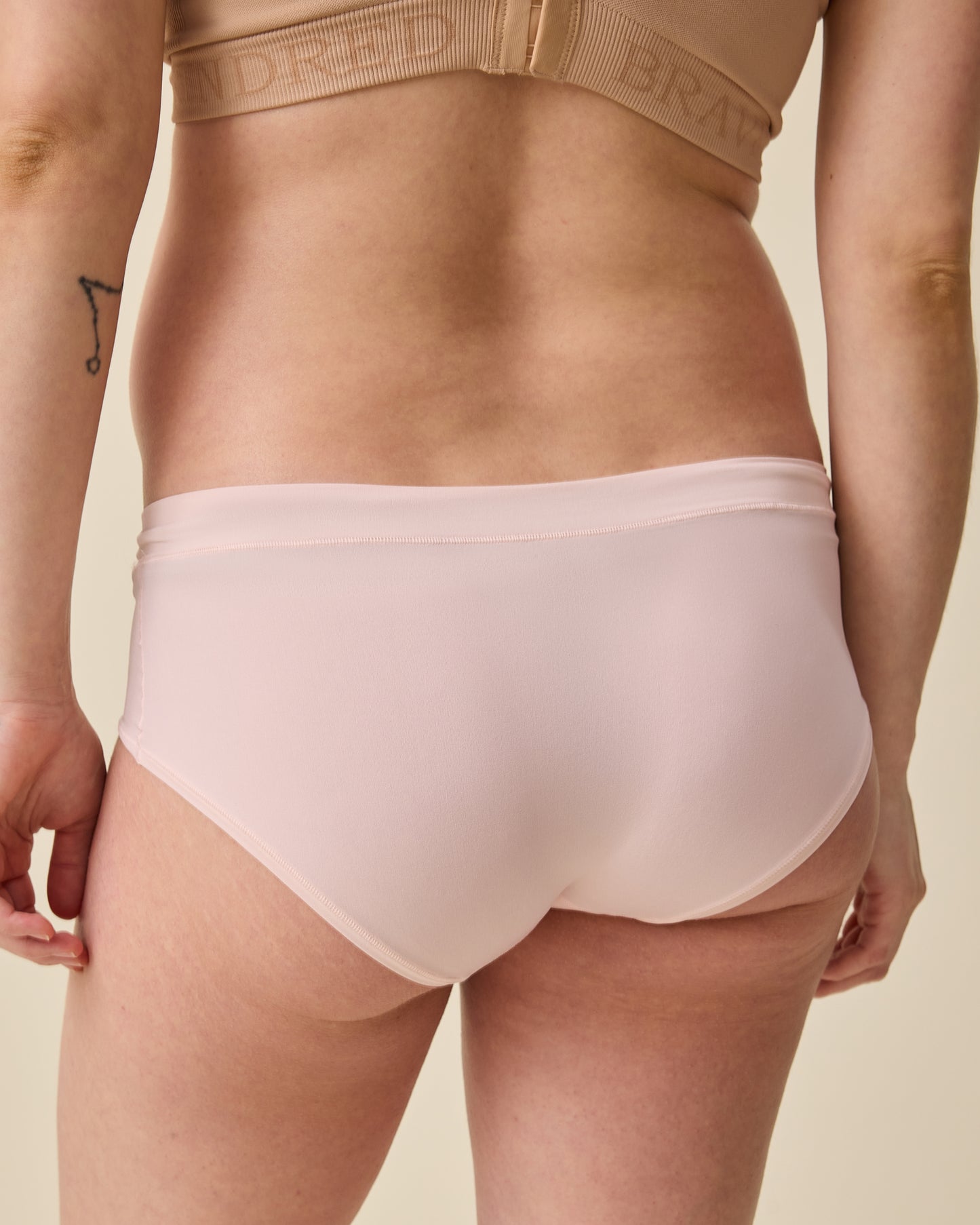 Back view of model wearing Grow with Me™ Maternity & Postpartum Hipster in Soft Pink on a beige background