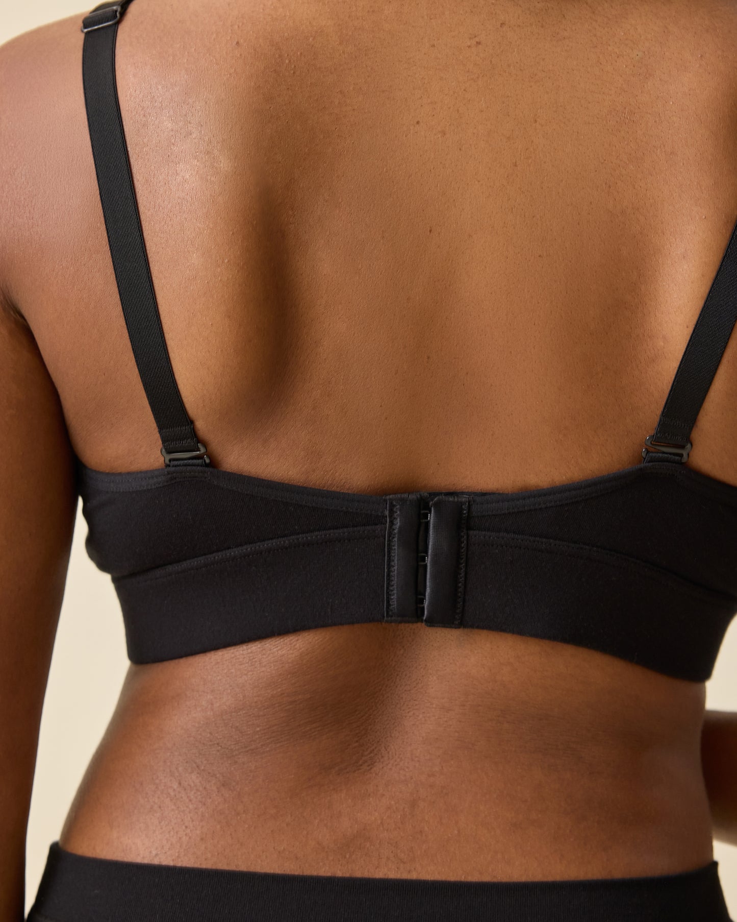 Back view of model wearing Every Stage Nursing Bra in Black on a beige background