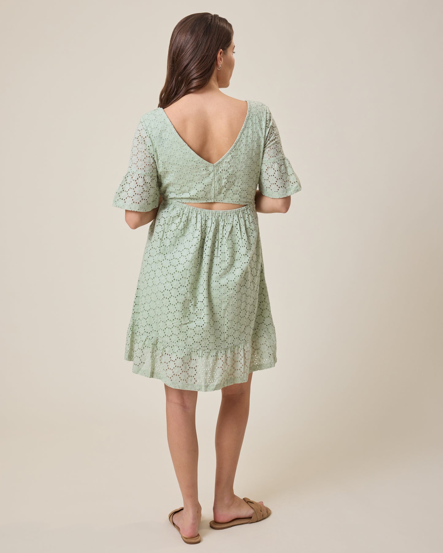 Woman wearing the Dahlia Eyelet Maternity & Nursing Dress in aqua mist with a subtle pattern on a beige background