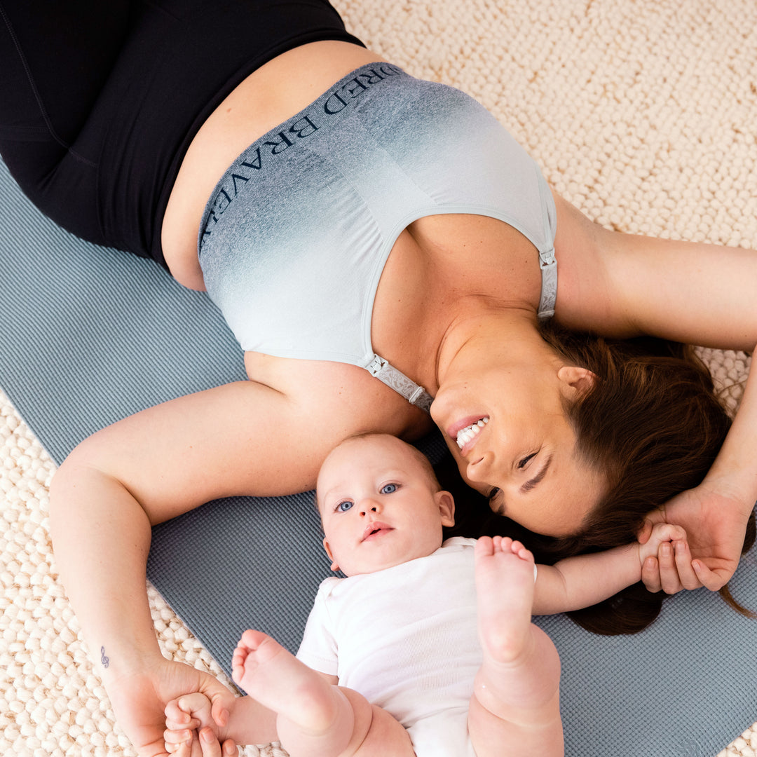 Model laying down on a yoga mat, wearing the Sublime® Nursing Sports Bra in ombre storm