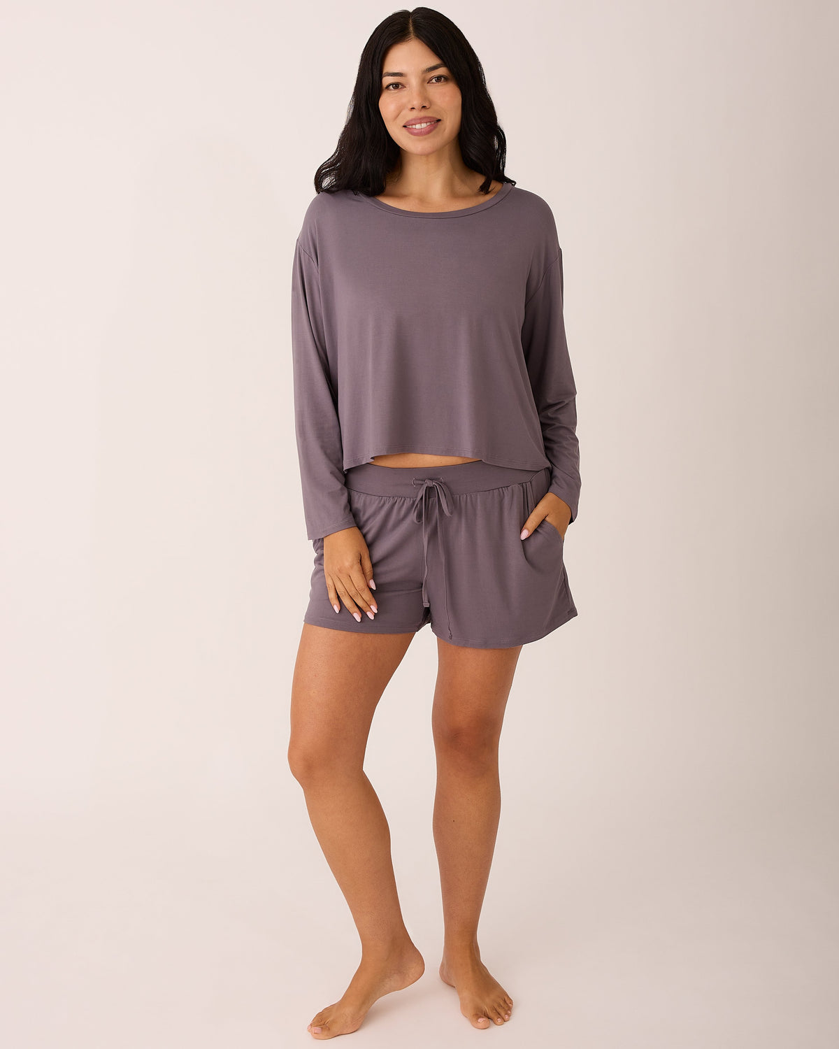 Model is wearing Aria Bamboo Casual Cropped Long Sleeve Top in Granite and Aria Bamboo Casual Lounge Short in Granite on a beige background.