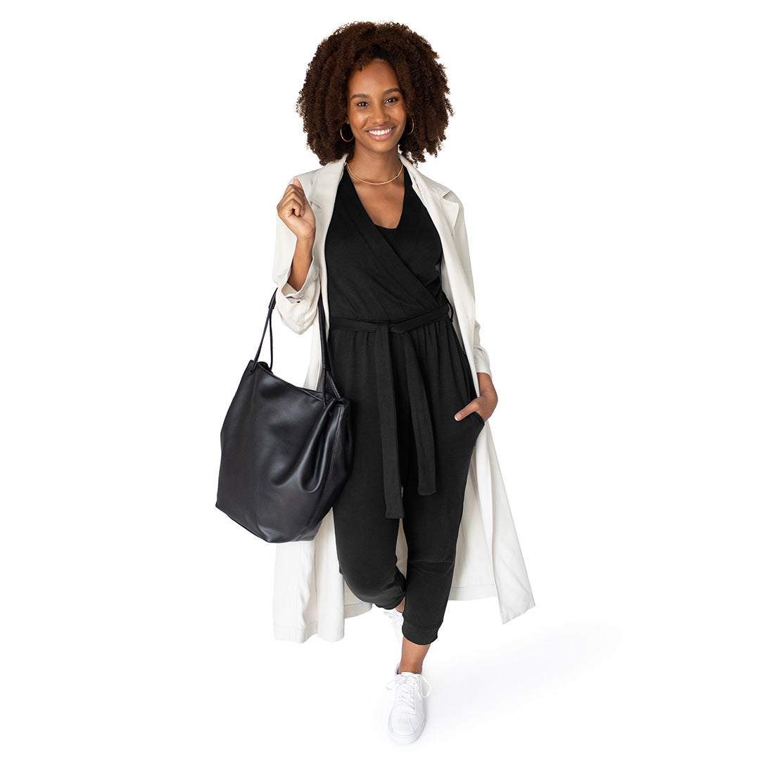 Model wearing the Around the Clock Nursing Jumpsuit in Black holding a black leather bag.