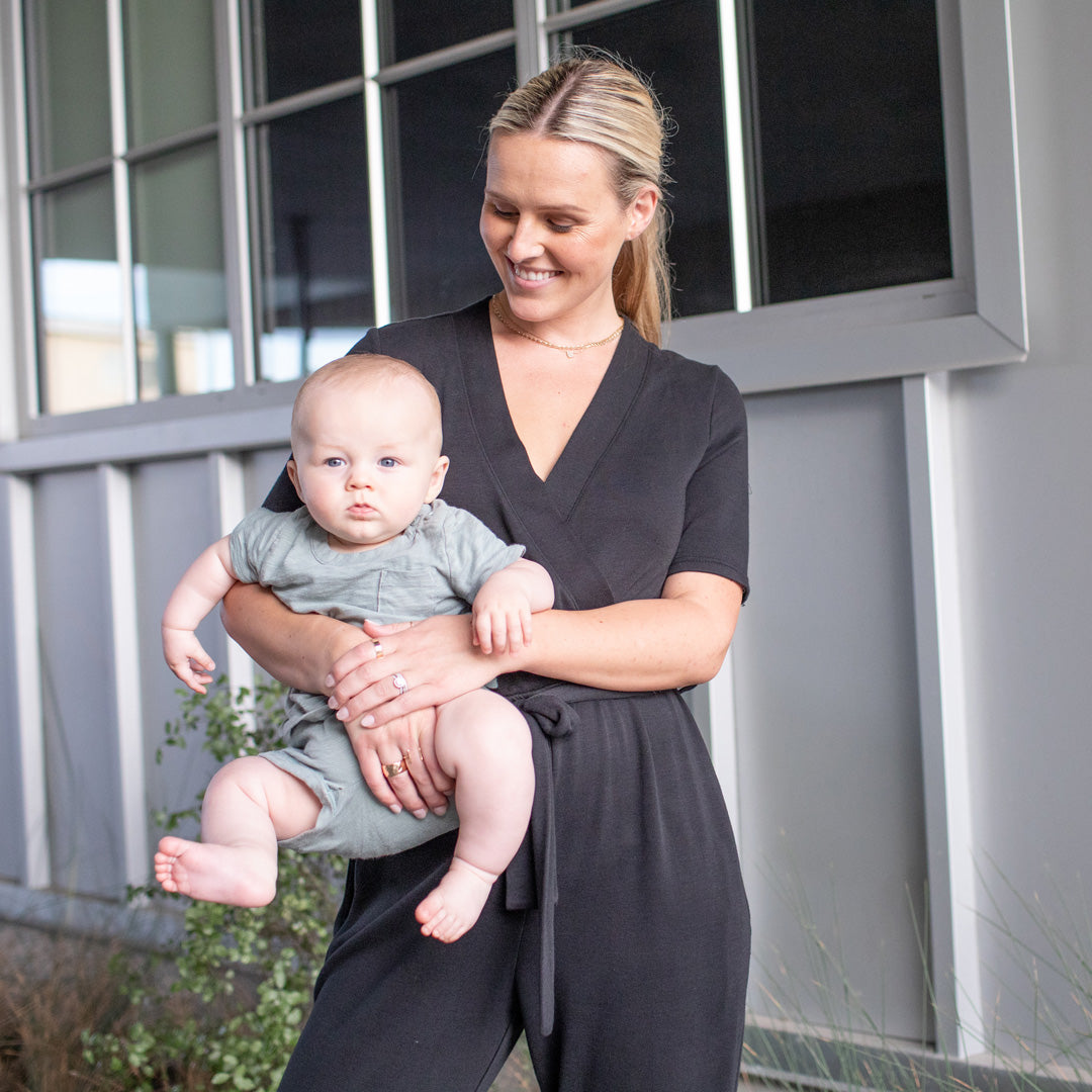 Model holding her baby while wearing the Around the Clock Nursing Jumpsuit in Black