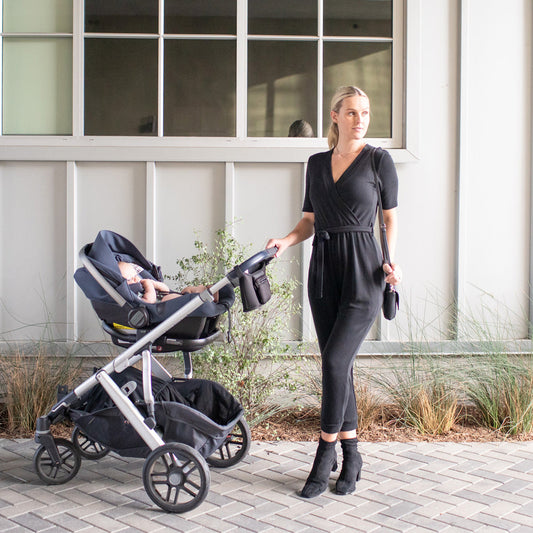 Model wearing the Around the Clock Nursing Jumpsuit in Black pushing her stroller. @model_info:Maddy is 5'8" and wearing a Small.