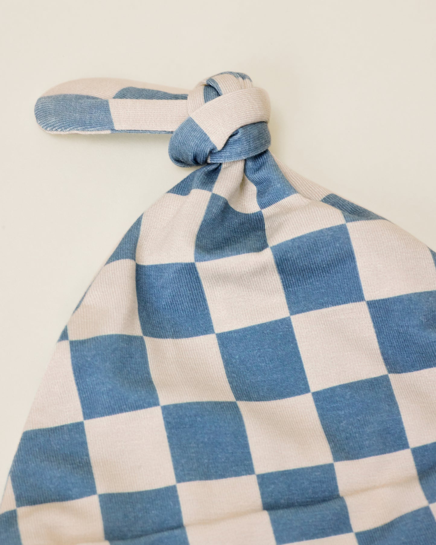 Close up of Bamboo Knotted Baby Gown & Hat in Blue Checker print on a neutral background, showing a detail of the hat