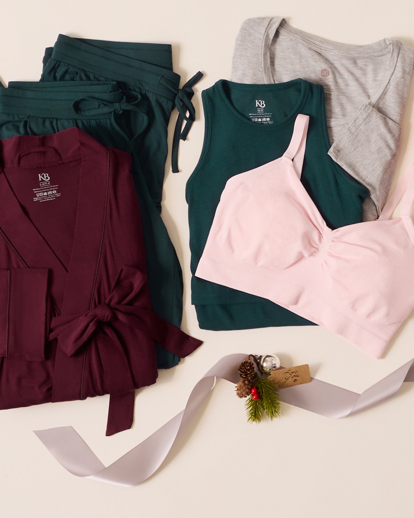 Collection of clothing including a robe, tank tops, and a top with a decorative ribbon and small gift on a light background.