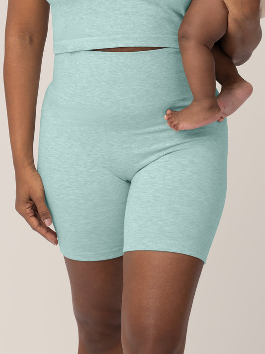 Model wearing the Sublime® Bamboo Maternity & Postpartum Bike Short in Dusty Blue Green Heather with her baby on her hip. @model_info:Rashé is 5’6" and wearing a Small.