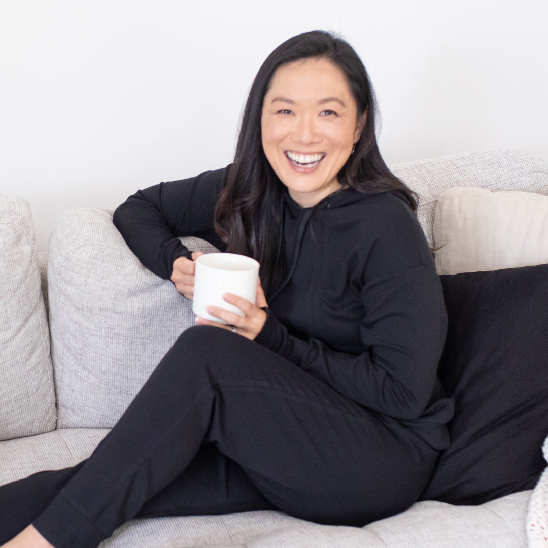 Model wearing the Bamboo Nursing Hoodie in Black sitting on a couch @model_info:Tiffany is wearing a Small.