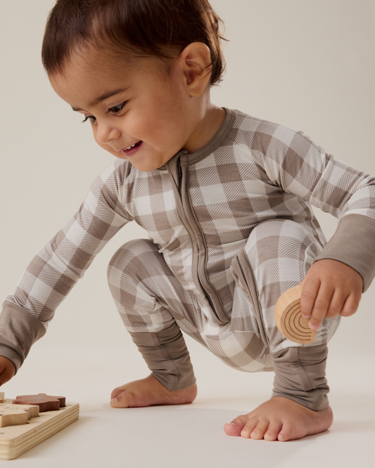 Baby wearing the Bamboo Baby Pajama in Taupe Gingham and playing with blocks@model_info:Delilah is wearing 3-6 months.