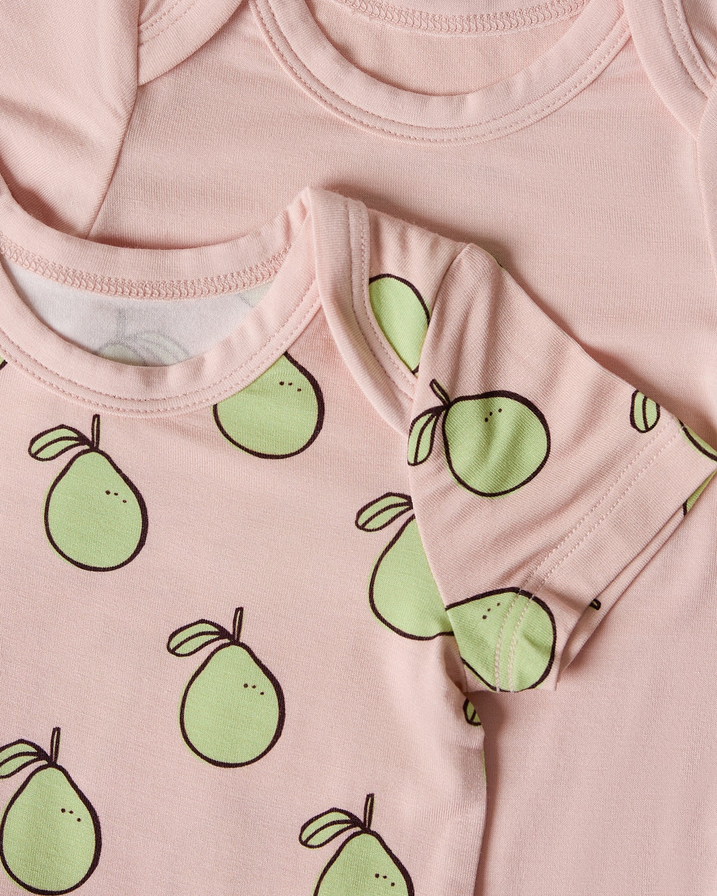Close-up of two pink baby onesies, one with green pomelo patterns
