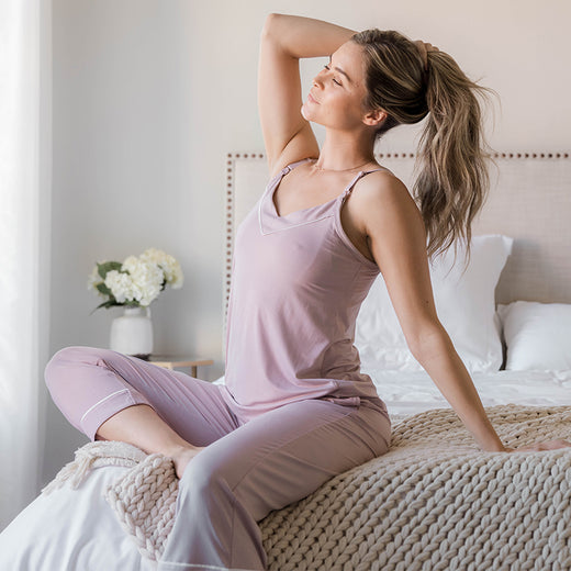 Model sitting on the edge of a bed wearing the Clea Tank Pajamas.