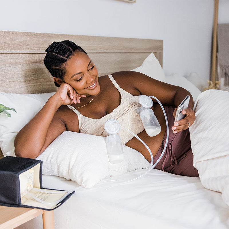 Model laying in a bed wearing a KB bra and pumping.
