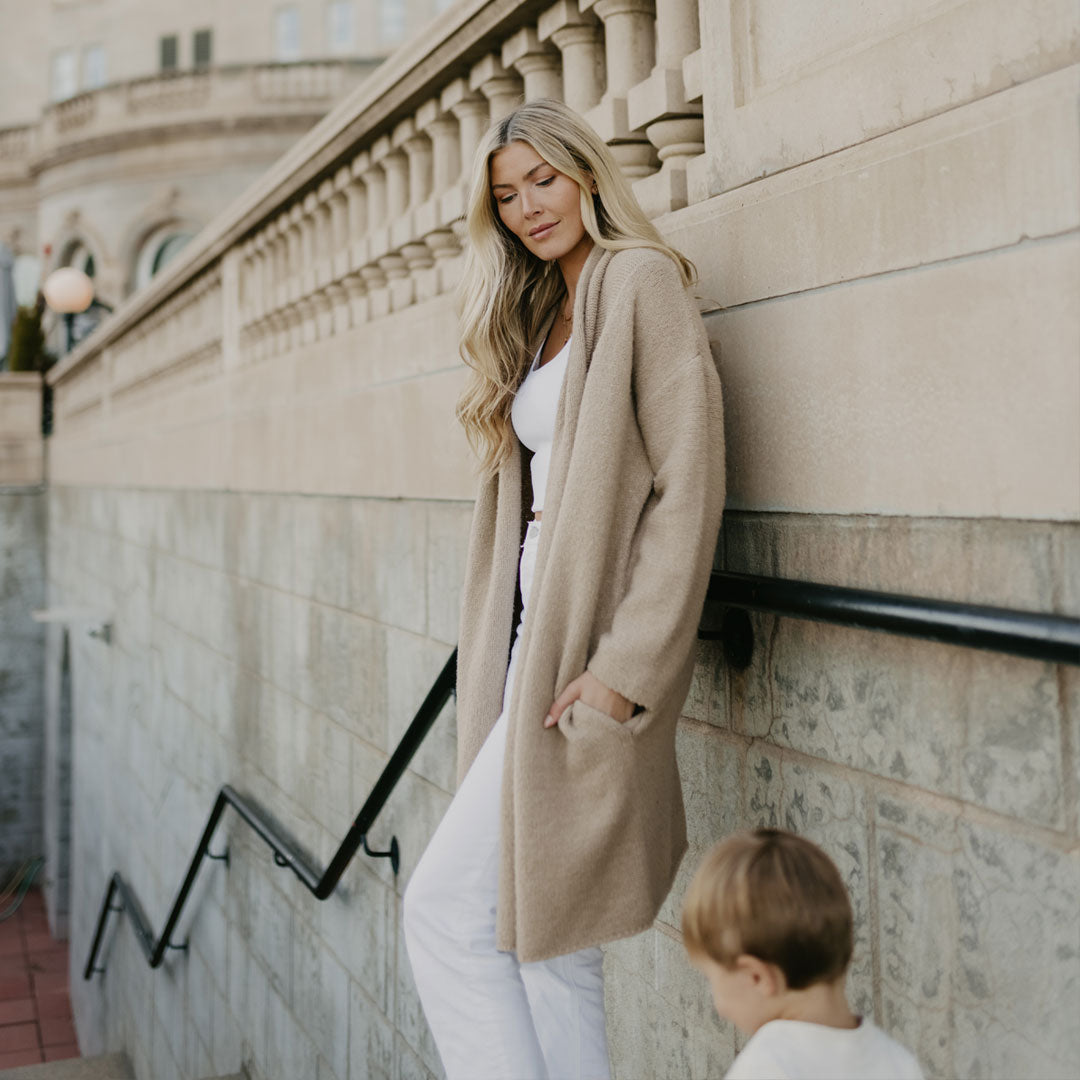 Model standing on stairs with her child wearing the Chloe Cardigan Sweater in Oat
