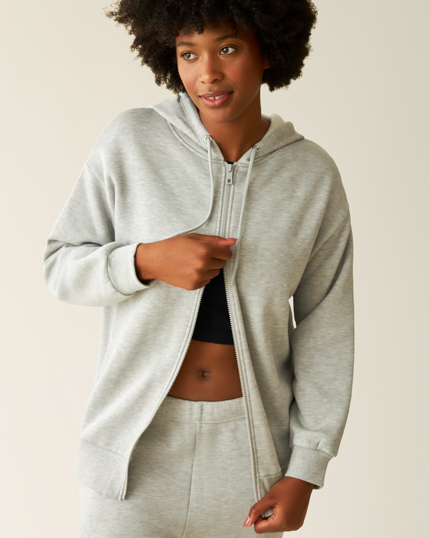 Woman wearing the Cloud Fleece Oversized Hoodie in Grey Heather with bottom zipper up @model_info:Kyra is wearing a Small.