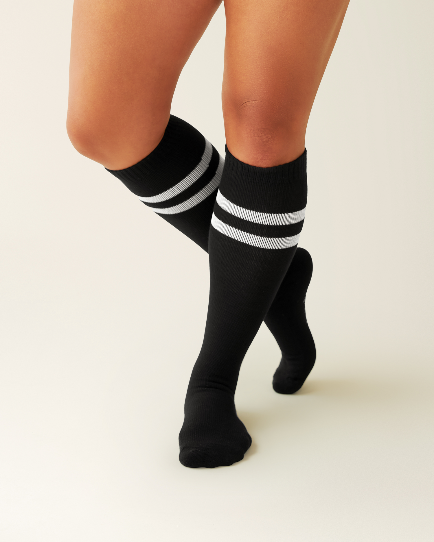 Black knee-high Premium Maternity Compression Socks with white stripes worn by a person on a beige background