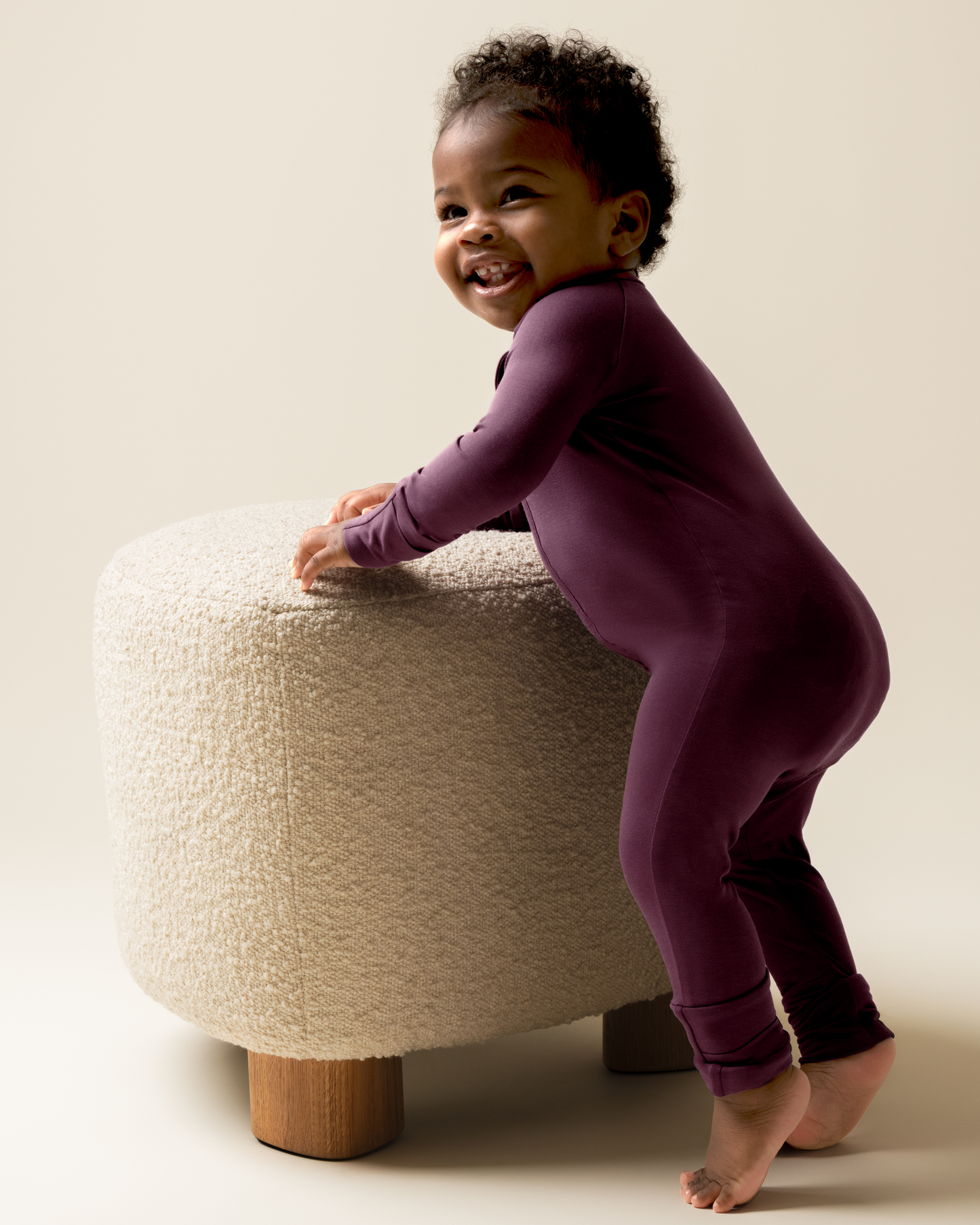 Child wearing Bamboo Baby Pajamas in Burgundy Plum standing on a textured stool against a plain background
