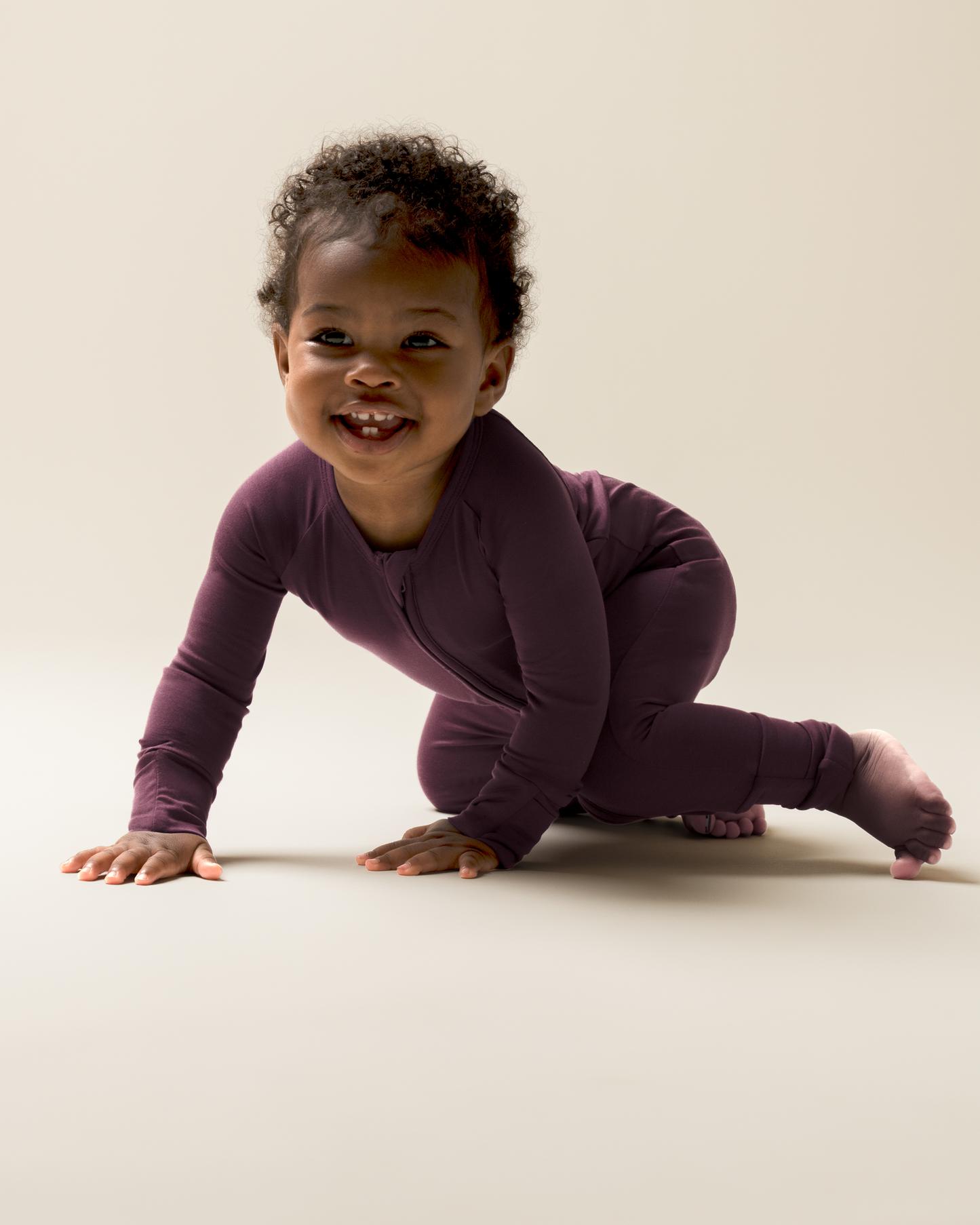 Child wearing Bamboo Baby Pajamas in Burgundy Plum against a plain background crawling on a light-colored floor.