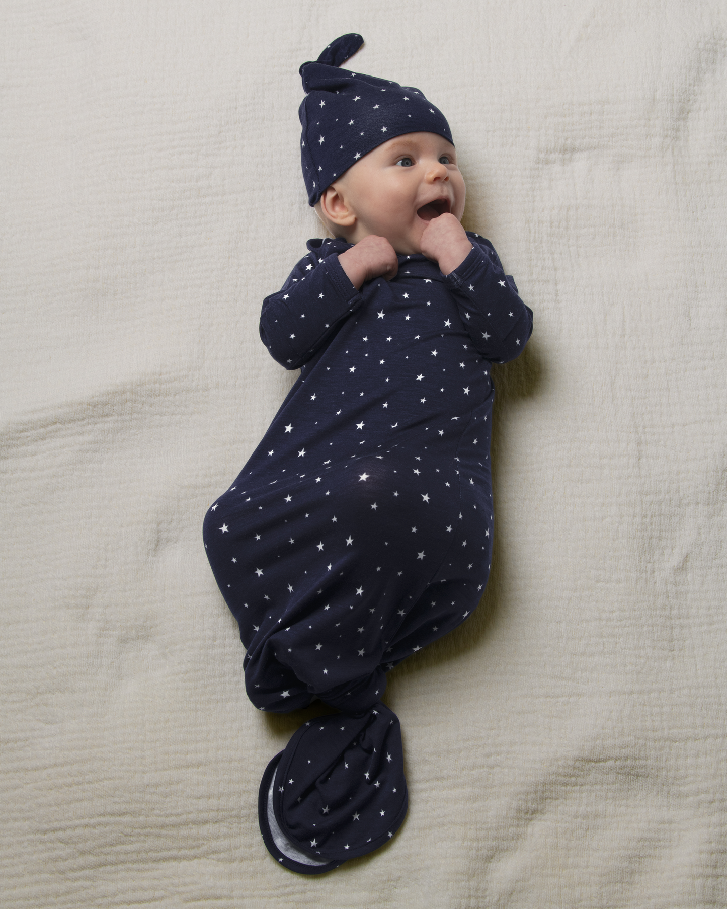 Baby wrapped in Bamboo Knotted Baby Gown in Navy Stars on a beige blanket@model_info:Danny is 3 months old.