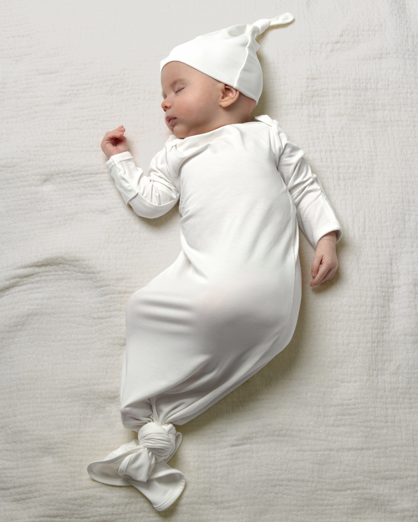 Baby in Bamboo Knotted Baby Gown in Pearl lying on a light gray surface@model_info:Danny is 3 months old.