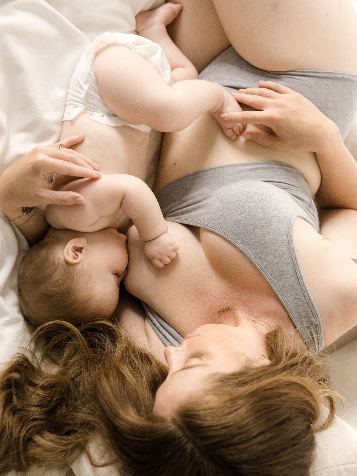 Model laying on bed wearing the French Terry Racerback Nursing & Sleep Bra in grey heather and nursing babt