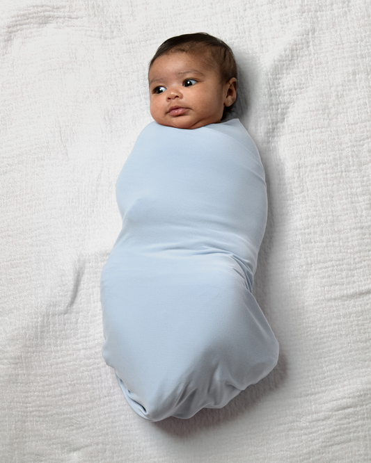 Baby wrapped in Bamboo Swaddle Blanket in French Blue on a white blanket@model_info:Luna is 6 weeks old.