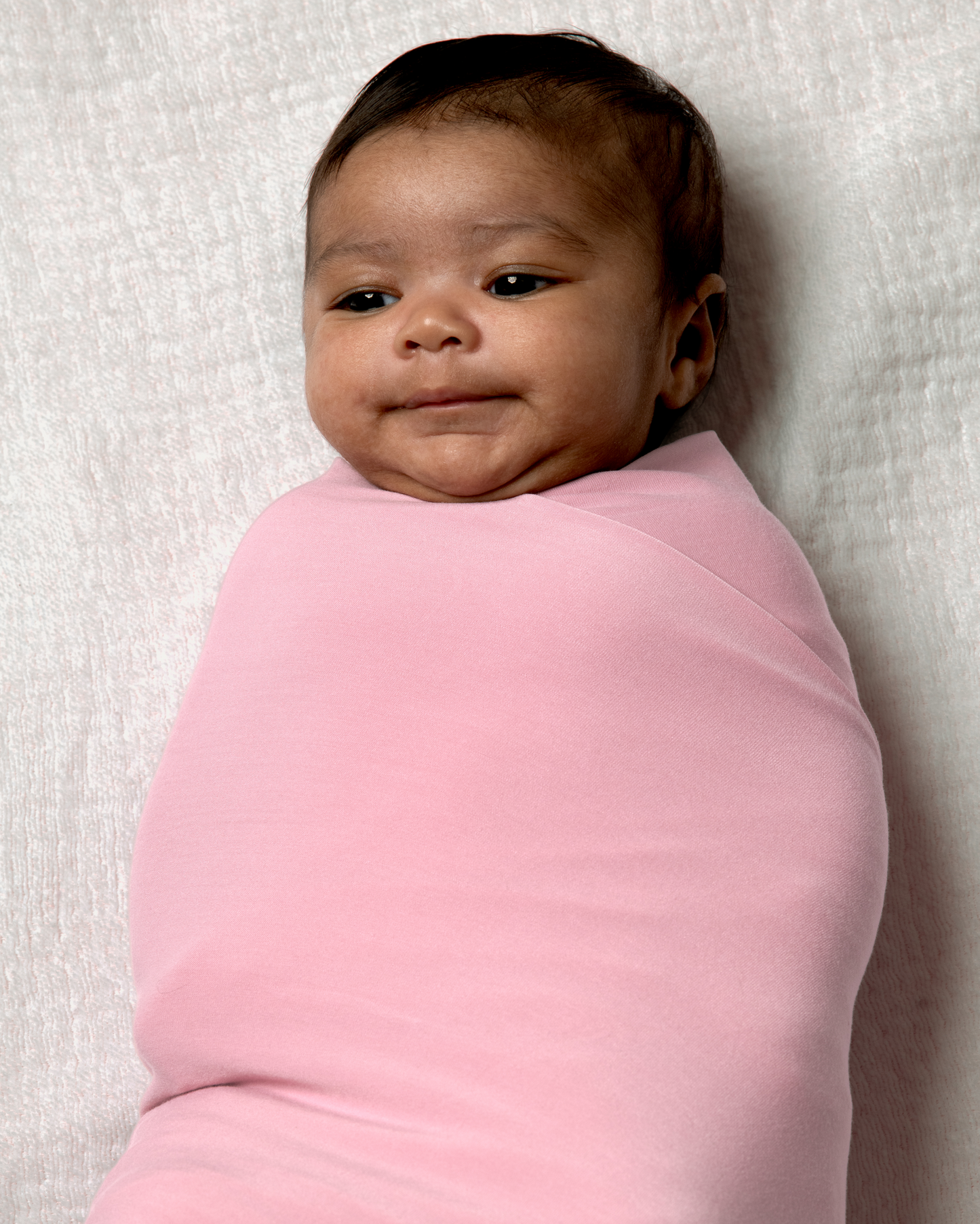 Baby wrapped in Bamboo Swaddle Blanket in Light Mauve on a white textured background